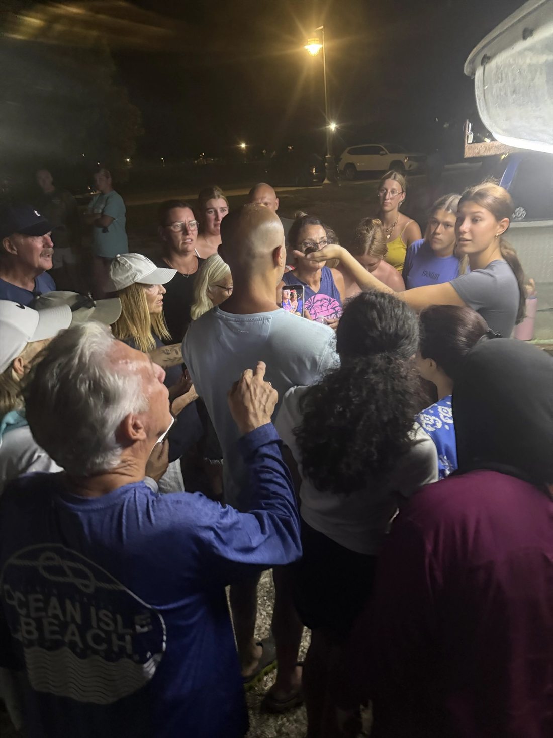 A guide holding up a creature found on the tour while a crowd of guests presses in around her on the beach at night